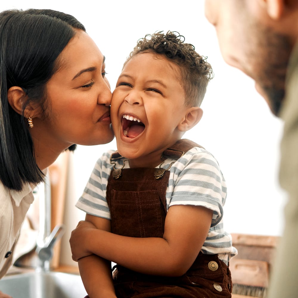 happy kid smiling while his mother is kissing him