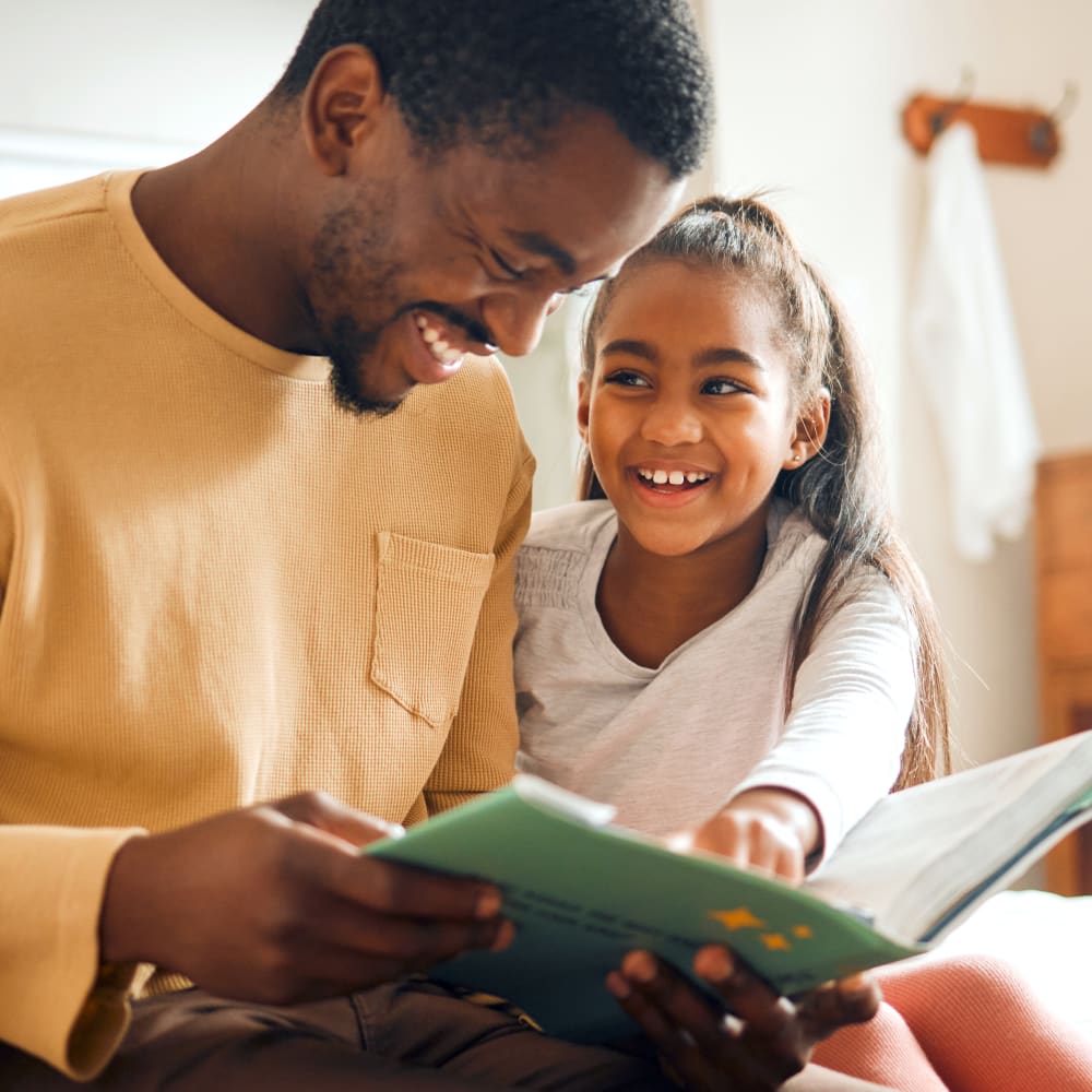 Father and daughter reading a book and smiling at orthodontics for children visit to Village Orthodontics