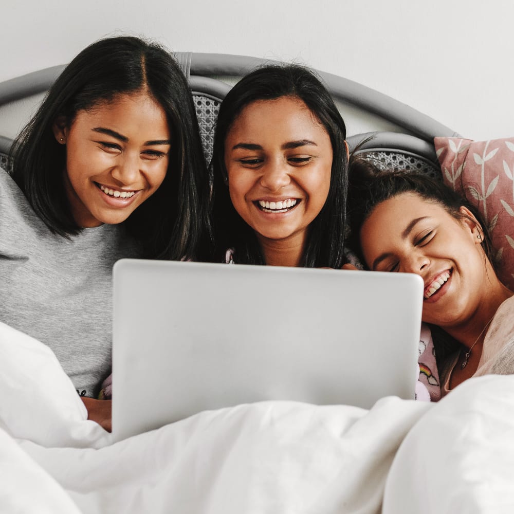 3 teenage girls smiling while watching a movie on a notebook after they got sleep apnea treatment